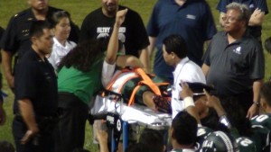 Aiea wide receiver Shaenen Hernandez-Fonoti raised his right arm as he was wheeled to the ambulance. (Paul Honda / Star-Advertiser)